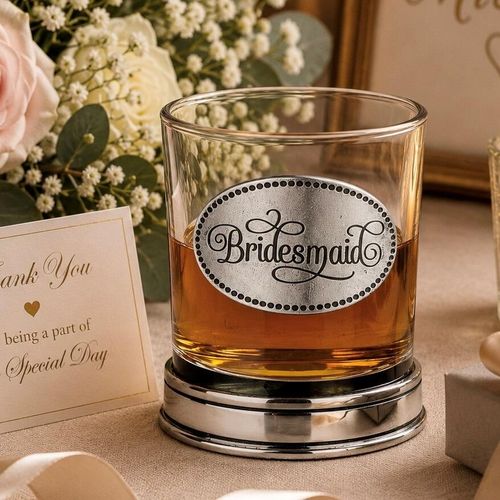 Whisky tumbler with pewter 'Bridesmaid' badge and polished base, partially filled with amber liquid