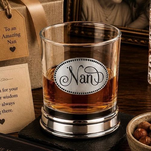 Whisky tumbler with pewter 'Nan' badge and polished base, partially filled with amber liquid