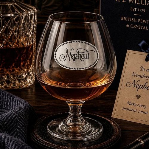 Elegant crystal brandy glass with pewter "Nephew" badge, partially filled with amber liquid