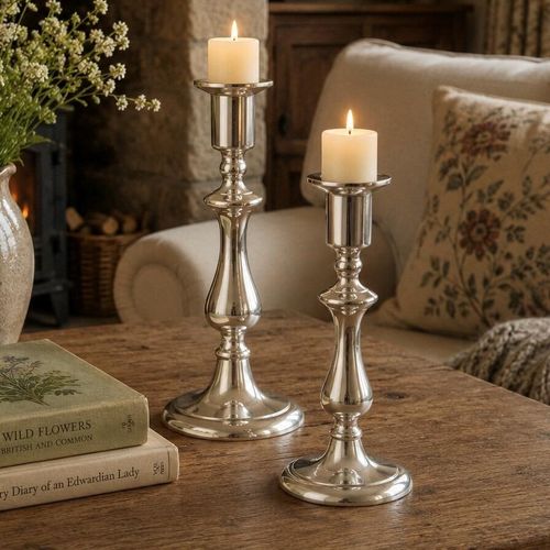 Pair of 8" high candlesticks with lit candles on a rustic wooden table in a cosy cottage