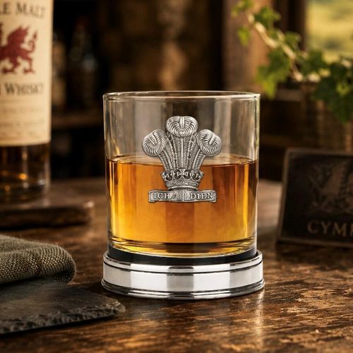 Whisky tumbler with pewter Welsh Feathers emblem and polished base, partially filled with amber liquid