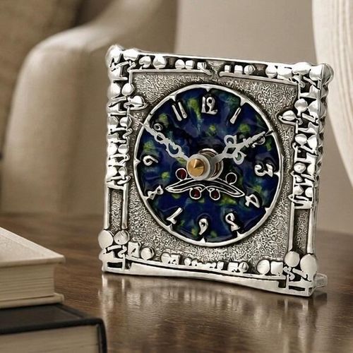A square pewter mantel clock in the style of Archibald Knox, featuring an intricate Celtic knotwork and organic openwork border, textured face, and a vibrant blue and green enamelled circular dial with stylized numerals
