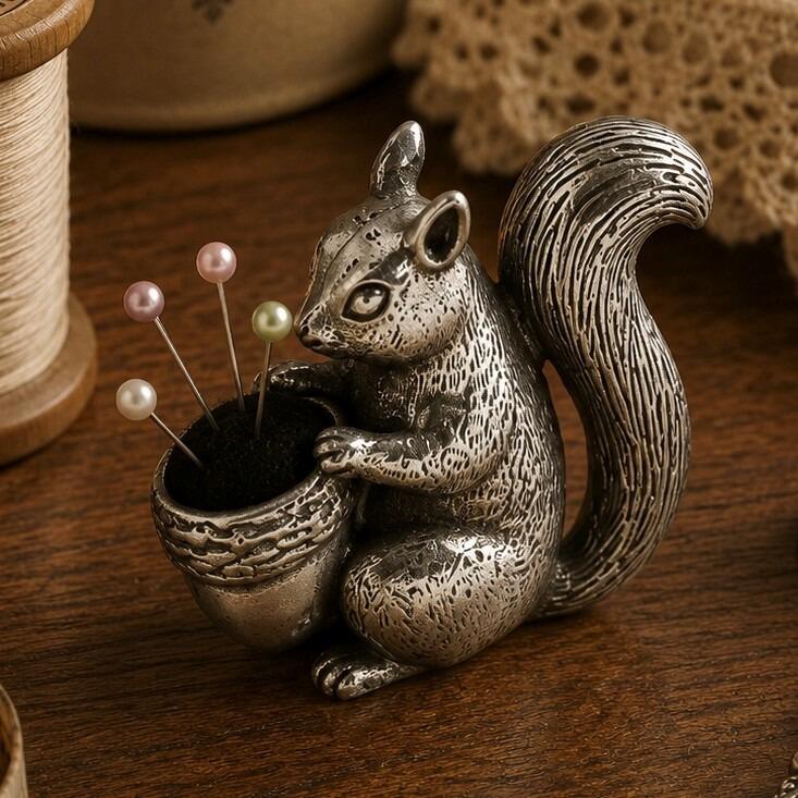 Detailed pewter squirrel pincushion figurine holding a large acorn with a black fabric cushion and four colorful pearl-head pins