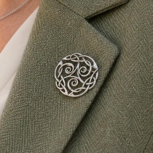 A circular pewter brooch featuring an intricate openwork Celtic triskele spiral and knotwork design