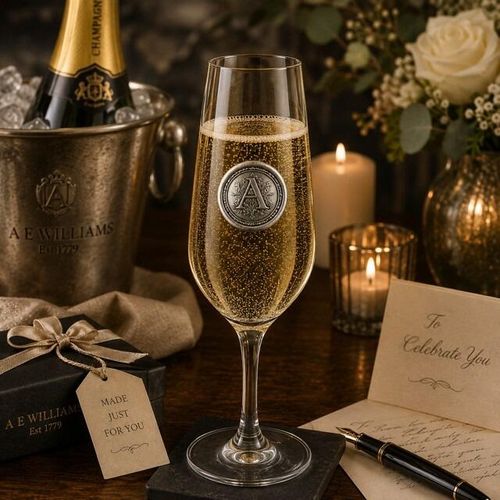 Champagne glass with a circular pewter emblem featuring the initial letter A, filled with sparkling wine