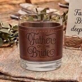 Glass tumbler wrapped in a brown stitched leather sleeve engraved with the words "Father of the Bride" in elegant script