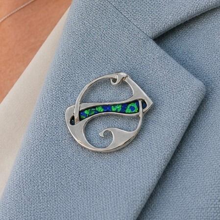 An Archibald Knox style pewter brooch featuring asymmetric Art Nouveau openwork loops and a central horizontal band of vibrant blue and green enamel