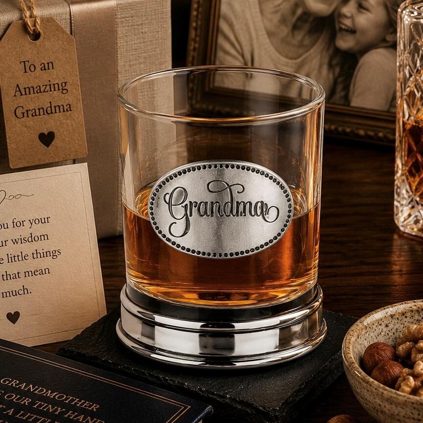 Whisky tumbler with pewter 'Grandma' badge and polished base, partially filled with amber liquid