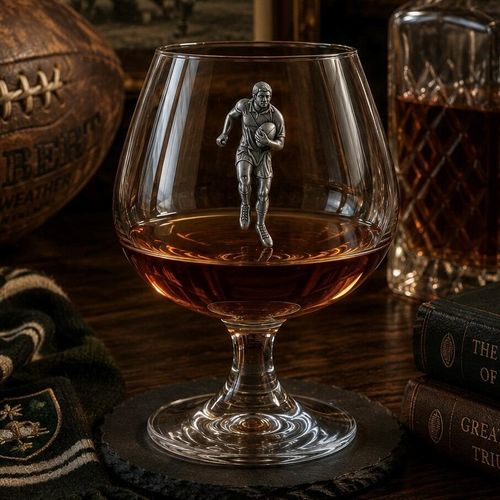 Crystal brandy glass with pewter rugby player emblem, partially filled with amber liquid