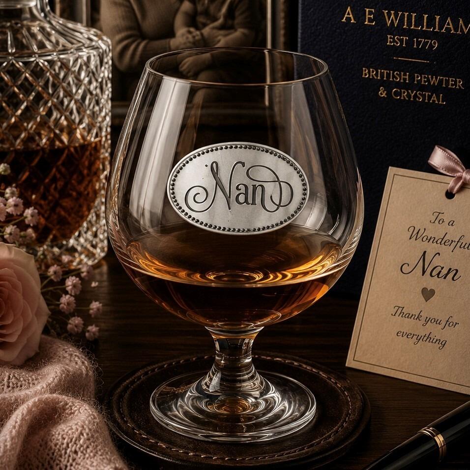 Elegant crystal brandy glass with pewter "Nan" badge, partially filled with amber liquid