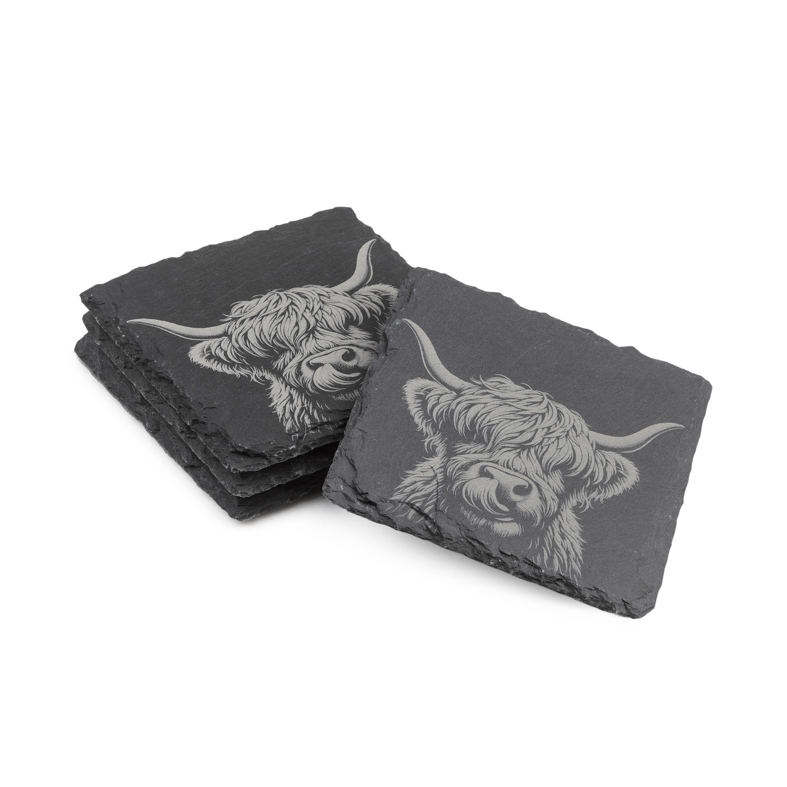 Two stacks of square slate coasters, each engraved with a detailed Highland Cow design.