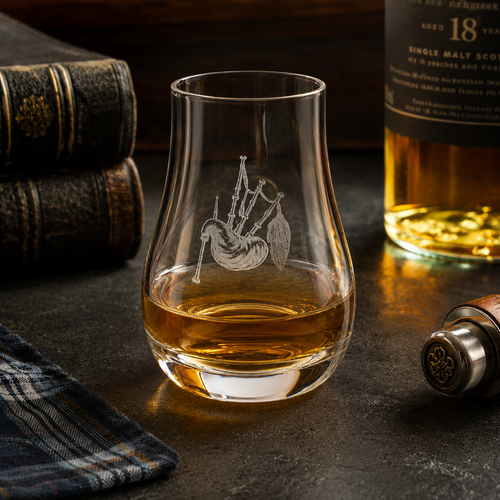 Crystal whisky tasting glass engraved with bagpipes, partially filled with amber Scotch whisky