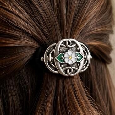 Elongated pewter Archibald Knox Art Nouveau style hair bobble featuring a central white enamel flower with a yellow center, flanked by green enamel leaves and openwork whiplash curves