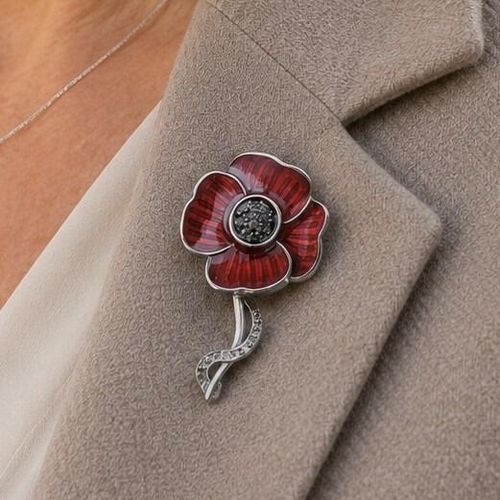 An Art Nouveau style pewter remembrance poppy brooch featuring vibrant red enameled petals, a textured dark center, and a curved stem engraved with the phrase "Lest We Forget"
