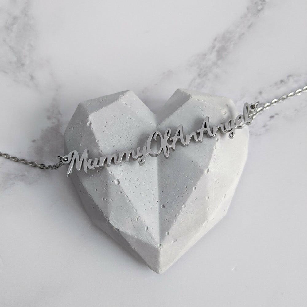 Mummy of an Angel necklace displayed on a decorative heart-shaped prop highlighting the script pendant