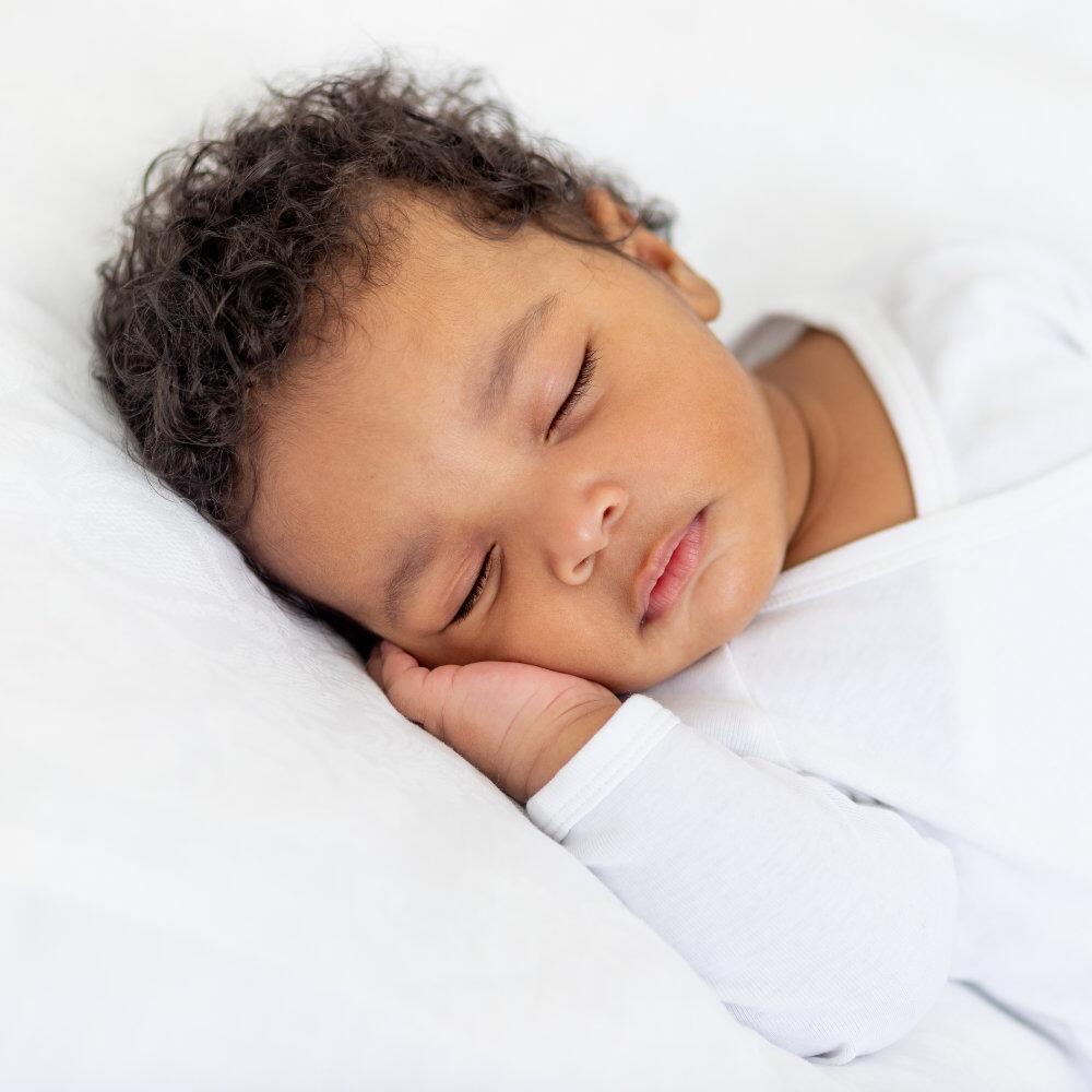 Child sleeping on a white cot bed pillow