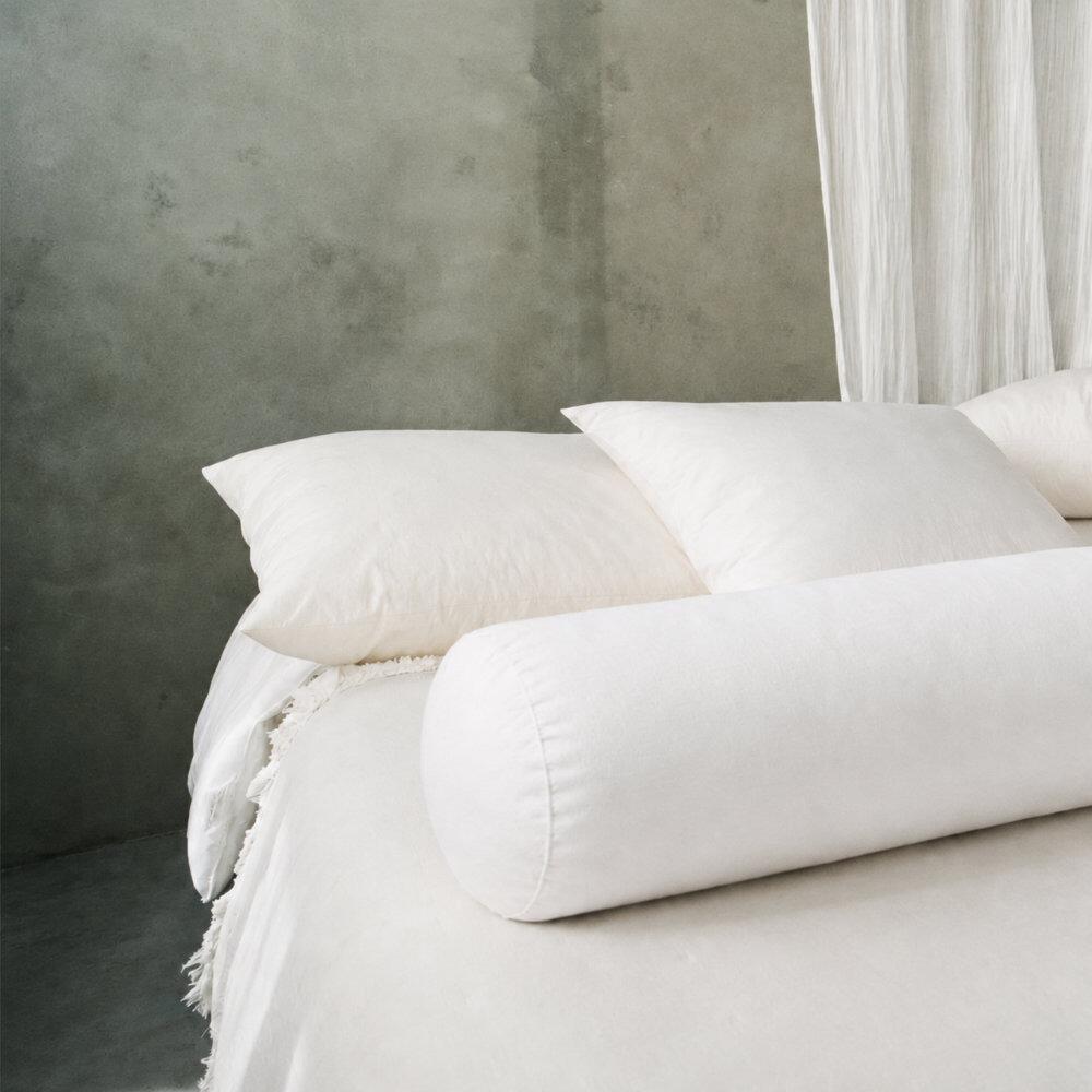 White wool bolster pillow shown on a bed