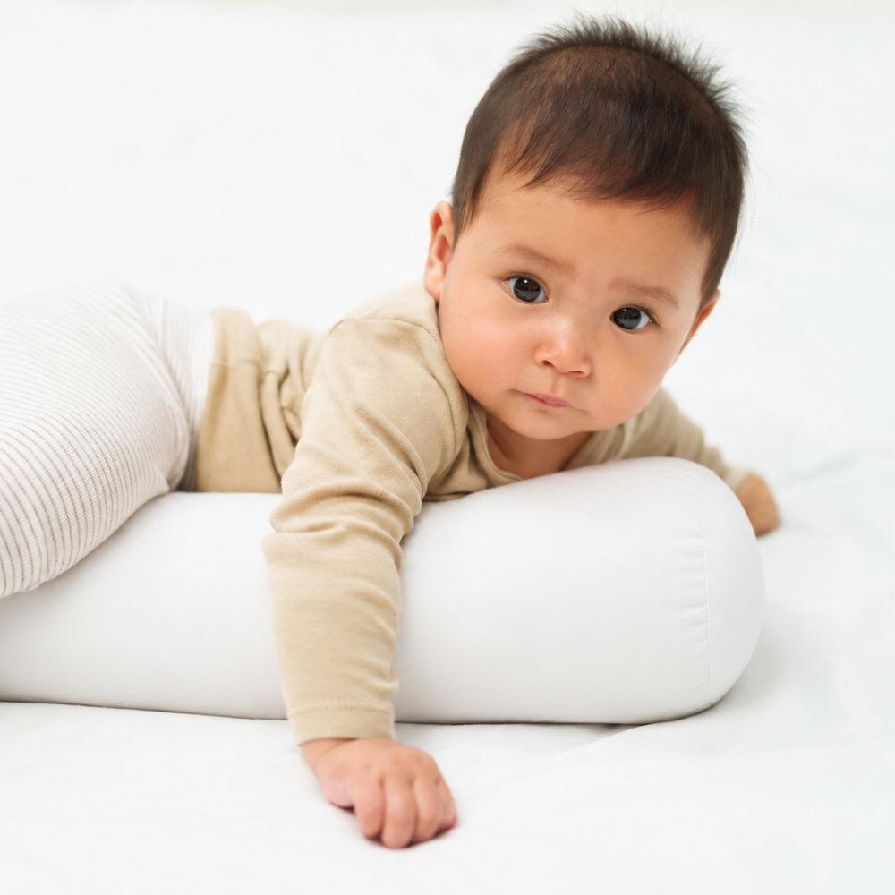 Baby leaning on a white baby bolster pillow