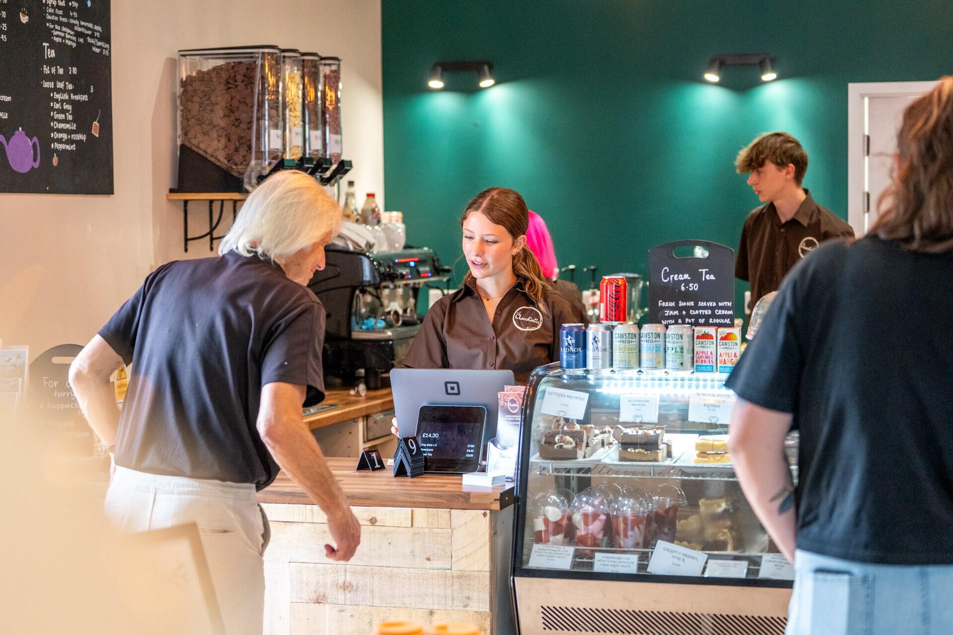 Heather, founder of Choccotastic, carrying a tray of hot chocolate and coffees in her Ledbury based Café.