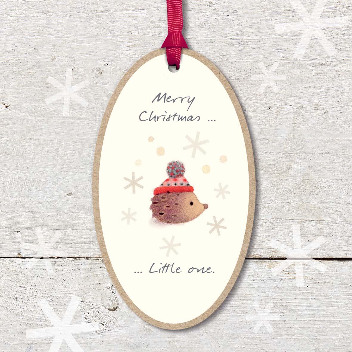 Large Christmas Wooden Plaque with attached red ribbon, featuring a cute baby hedgehog wearing a woolly hat, with a ’Merry Christmas Little one’ caption.