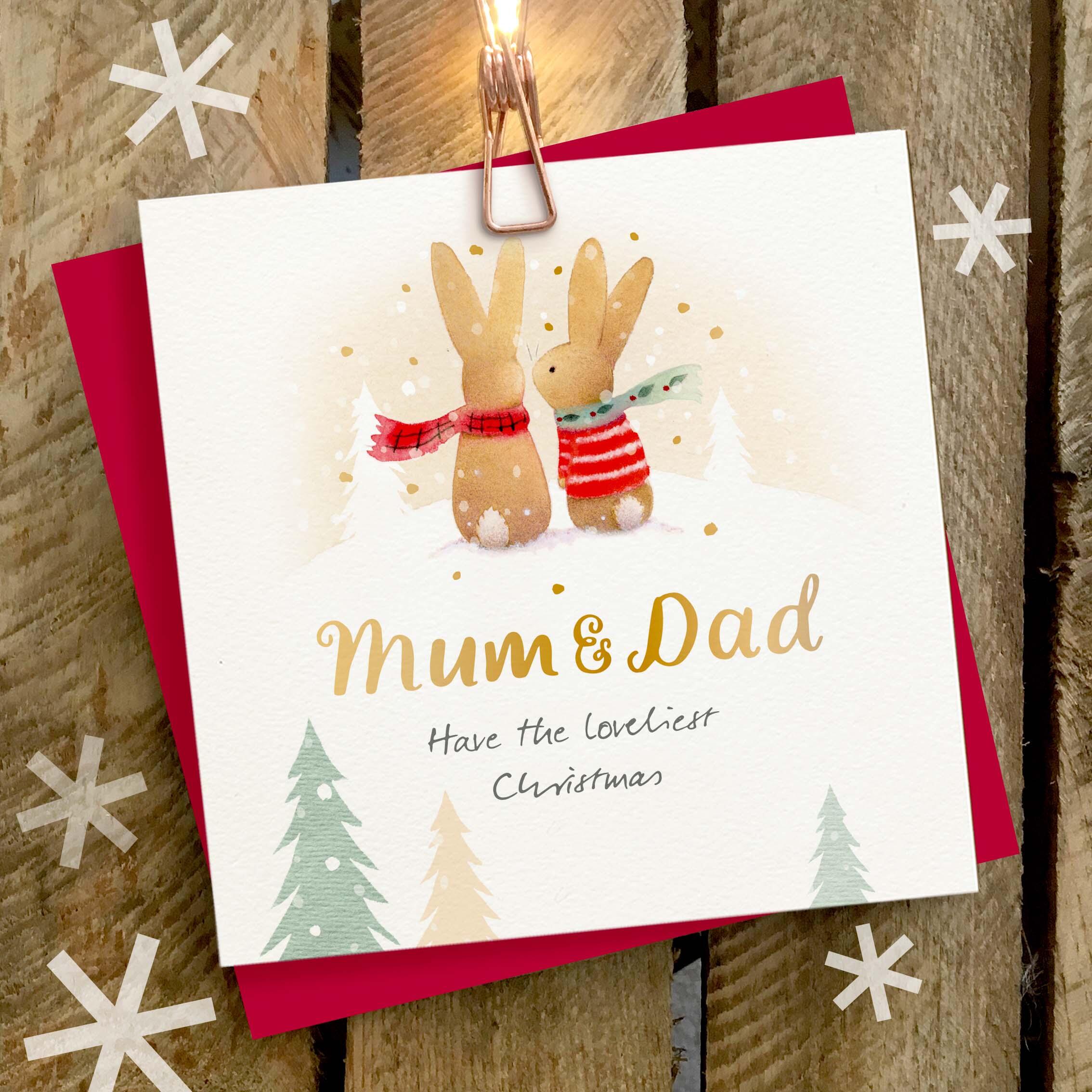 Christmas card featuring a large gold foil ‘Mum and Dad’ caption and a cute rabbit couple wearing woolly scarves.