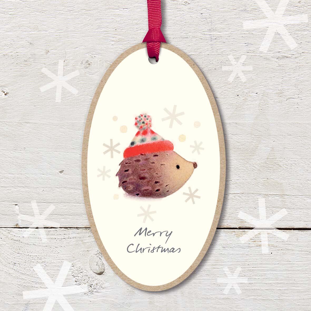 Large Christmas Wooden Plaque with attached red ribbon, featuring a cute hedgehog wearing a woolly hat, with a ’Merry Christmas’ caption.