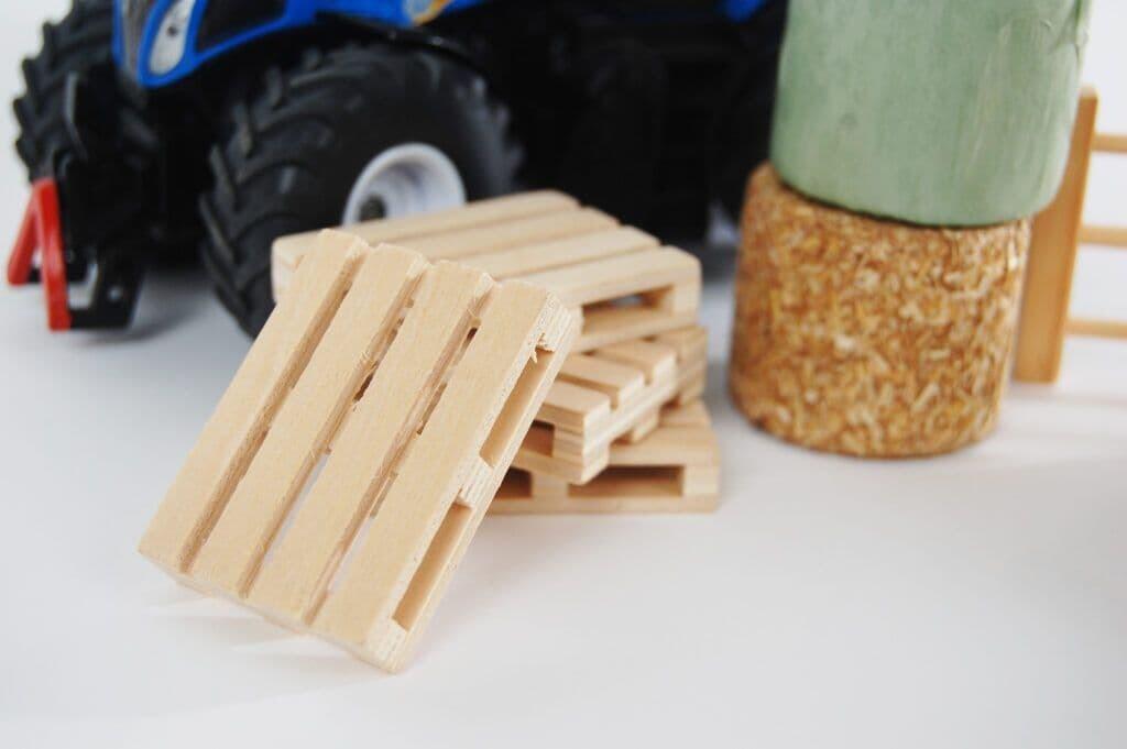 Kids Globe 1:32 farm accessories including pallets, barrels and small equipment placed on a toy farm setup.