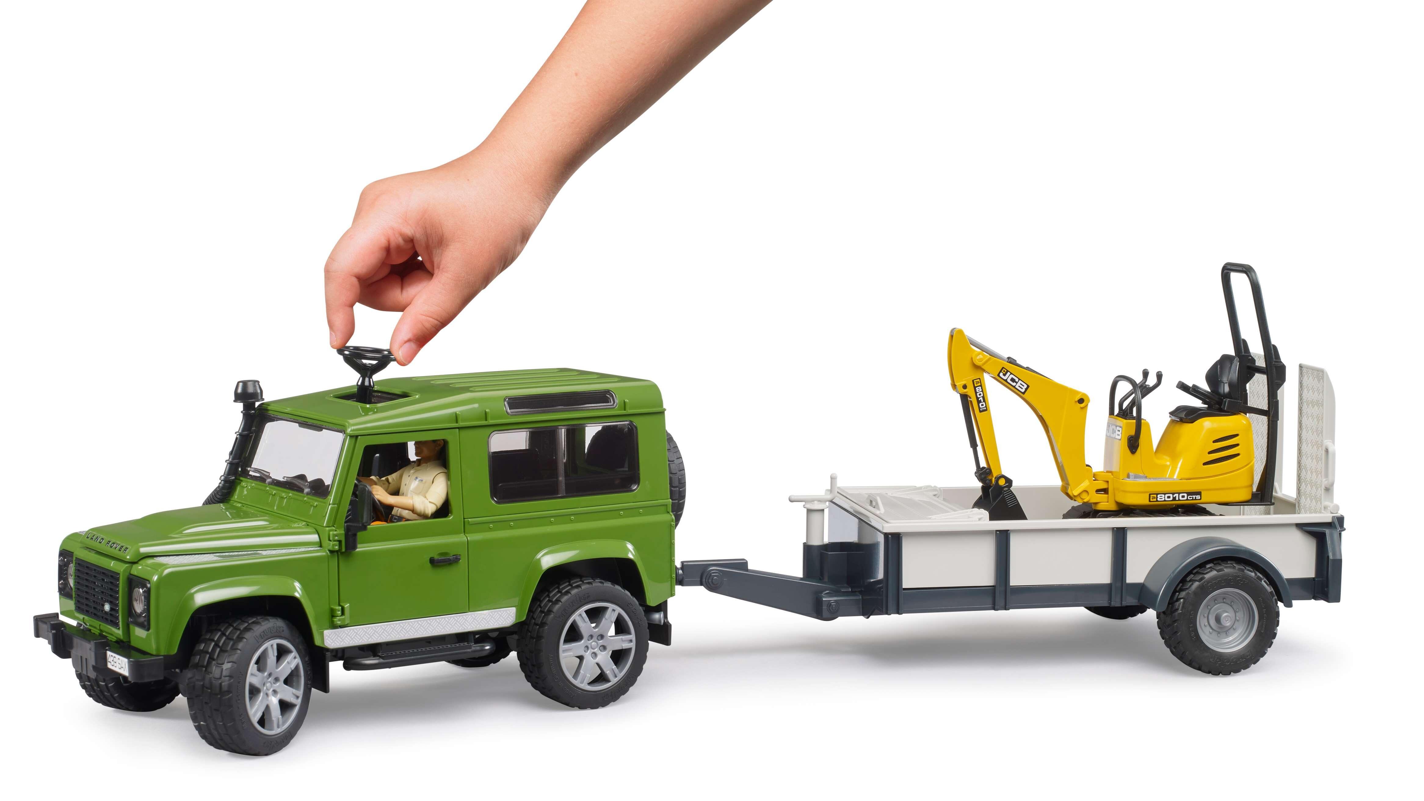 Hand placing figure into Bruder Land Rover Defender with trailer and JCB excavator