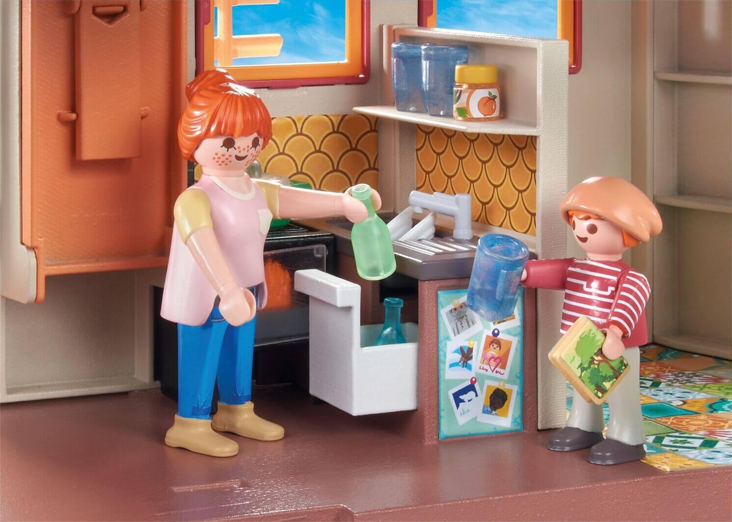 Close-up of the PLAYMOBIL Tiny House kitchen with two figures holding bottles and cups beside the sink and storage shelves.”