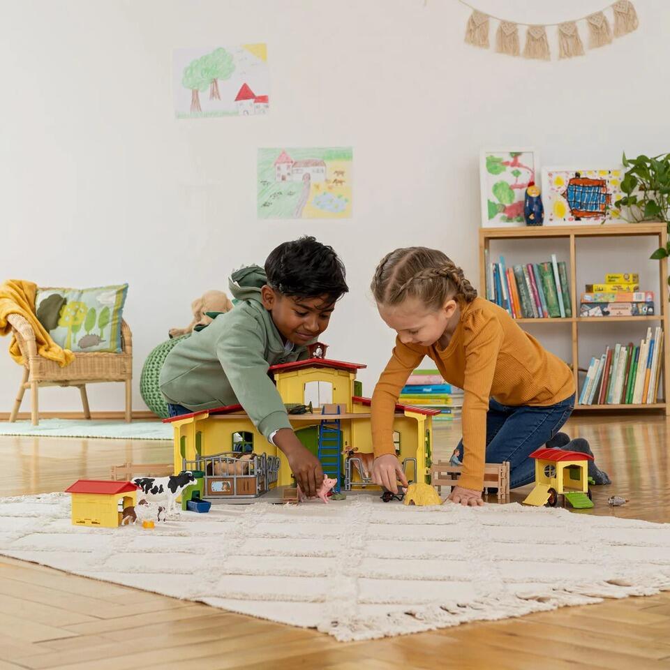 Two children playing with the Schleich Large Farm 42605 set on the floor.