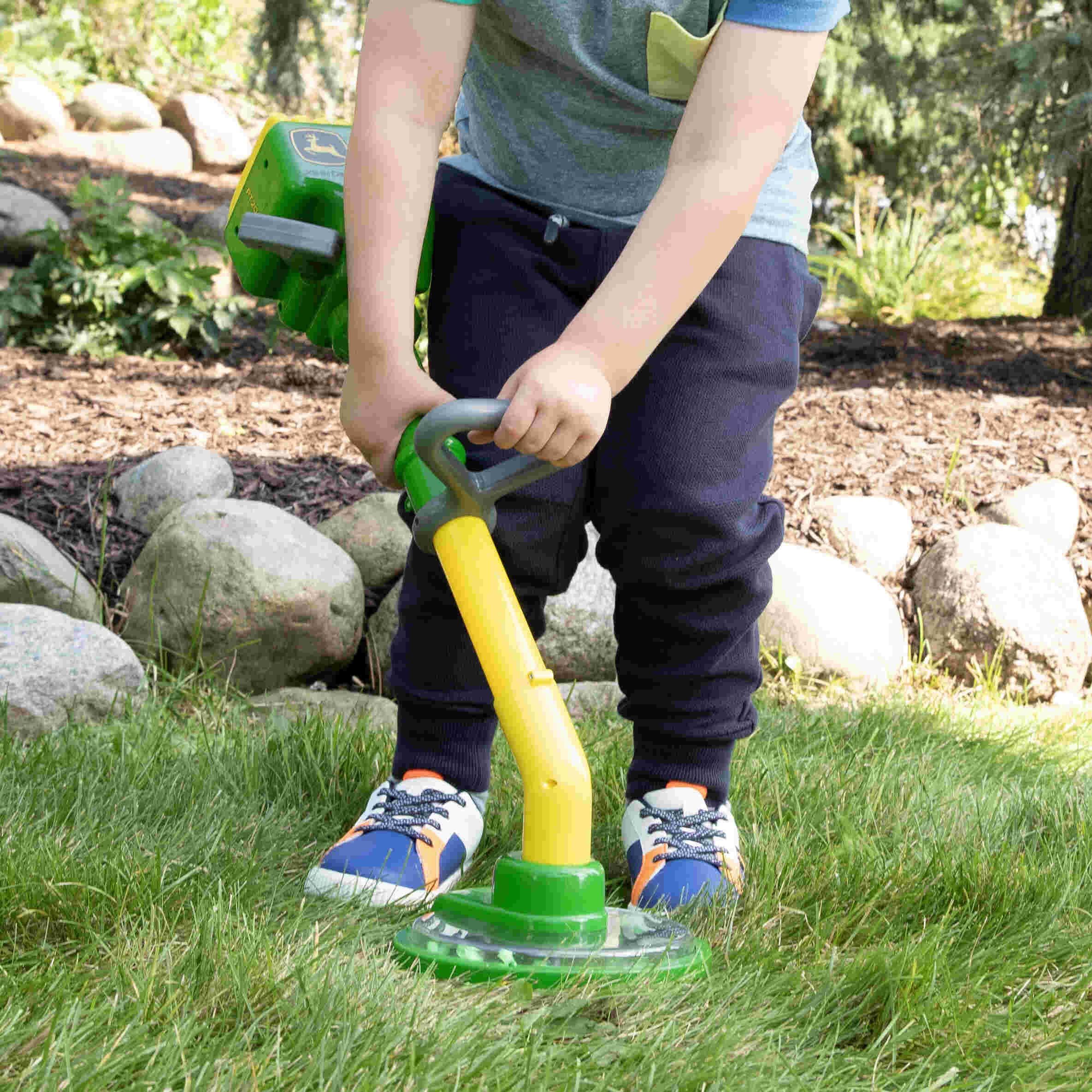 Child using a John Deere toy power trimmer outdoors on the grass.