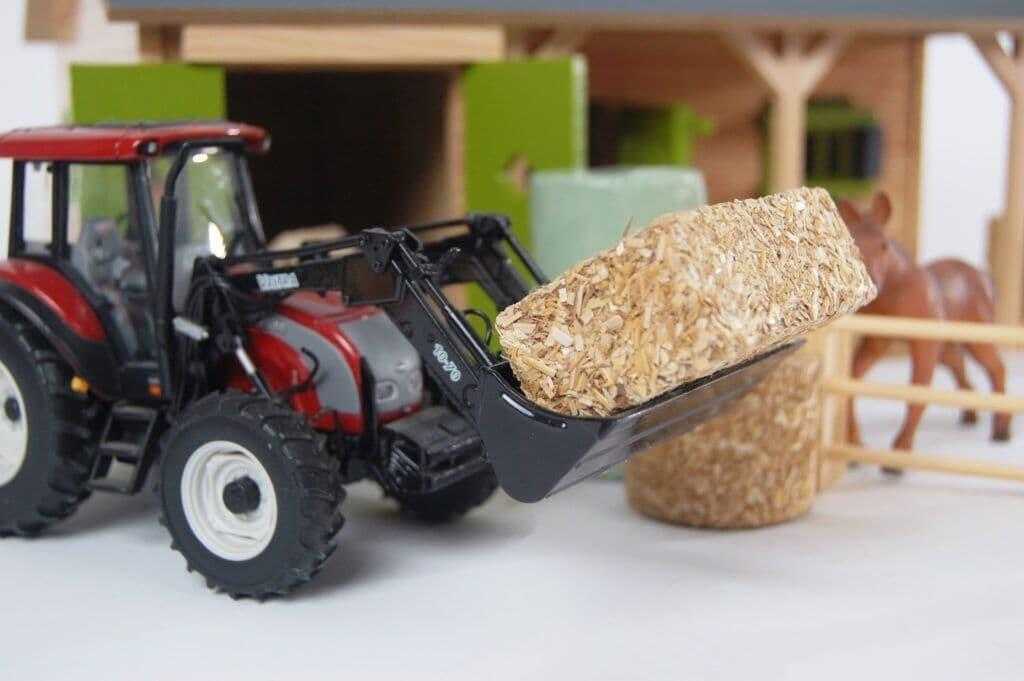 Close-up of Kids Globe 1:32 farm accessories arranged in front of a toy tractor in a farmyard scene.