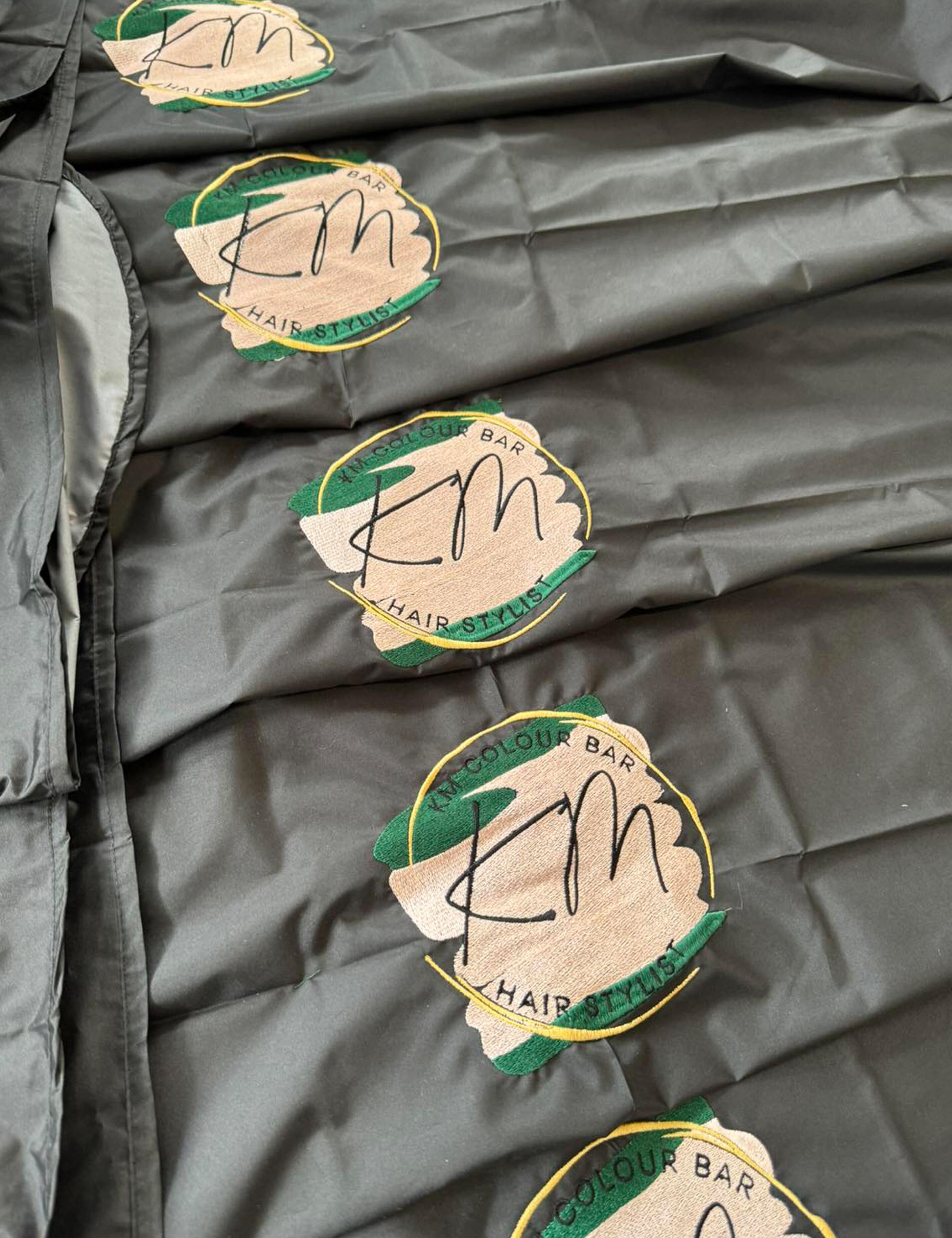 Black barber cape with hand slits featuring custom logo embroidery