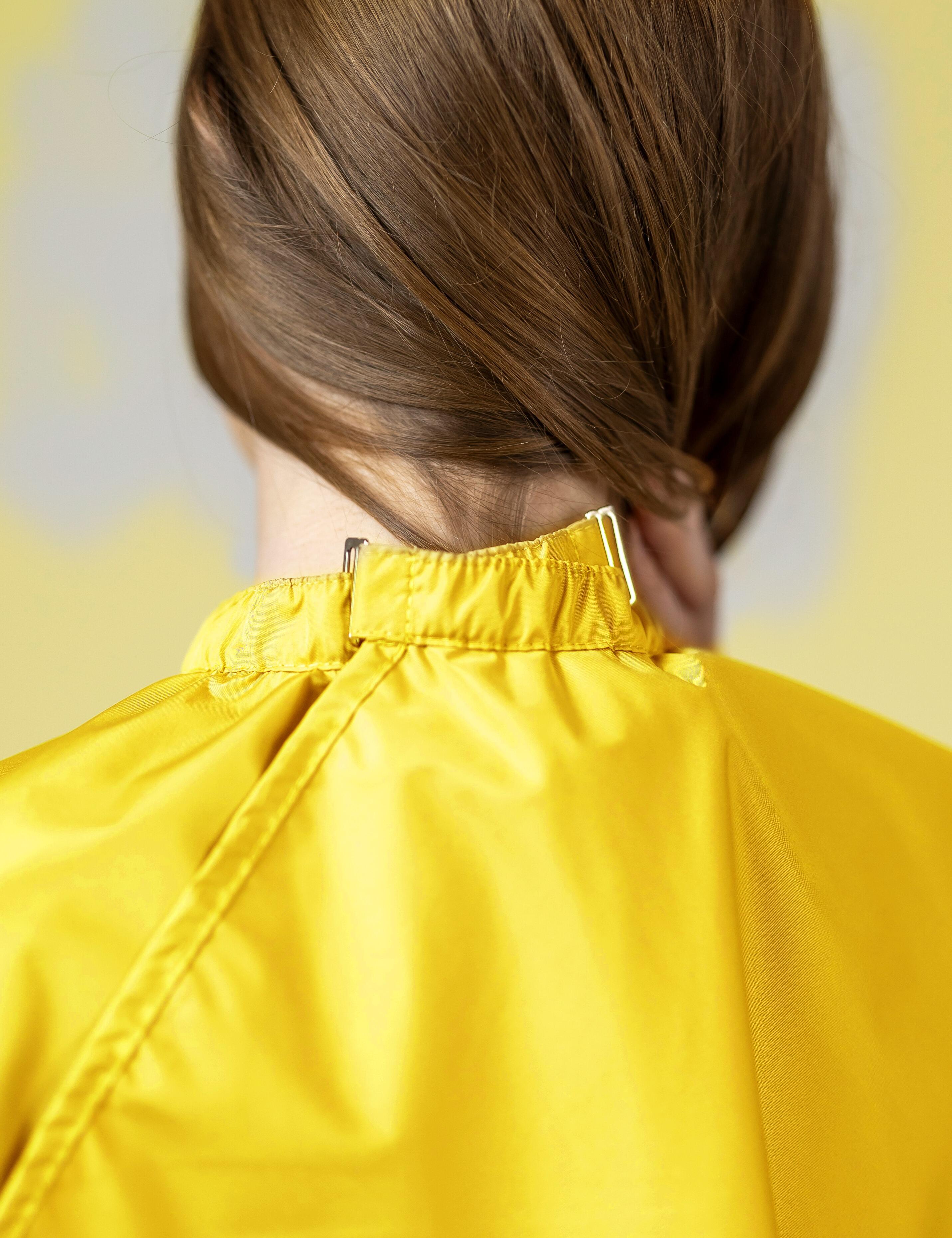 Yellow salon cape with hand slits and secure clip closure