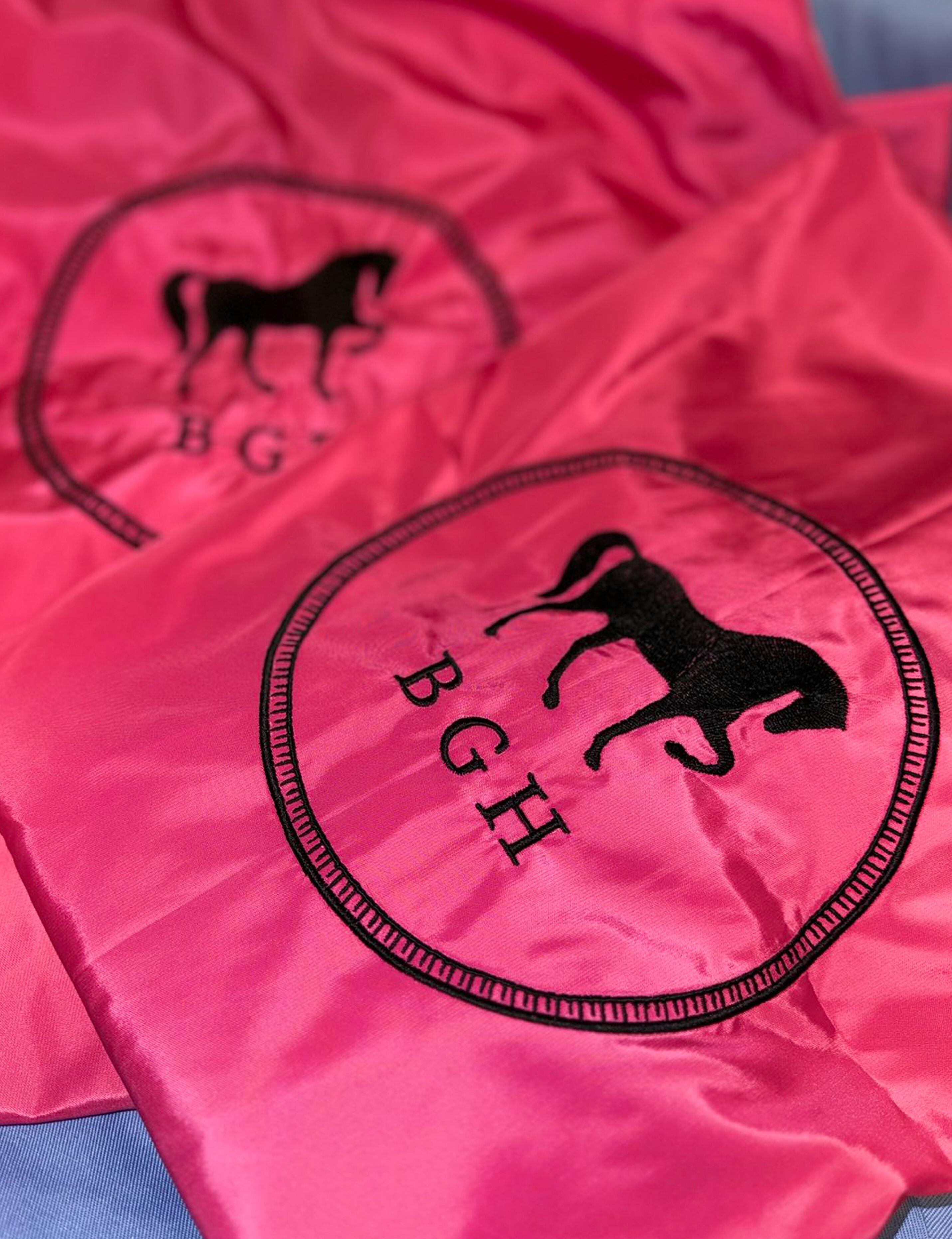 Premium embroidered hot pink salon cape featuring high-quality branding.