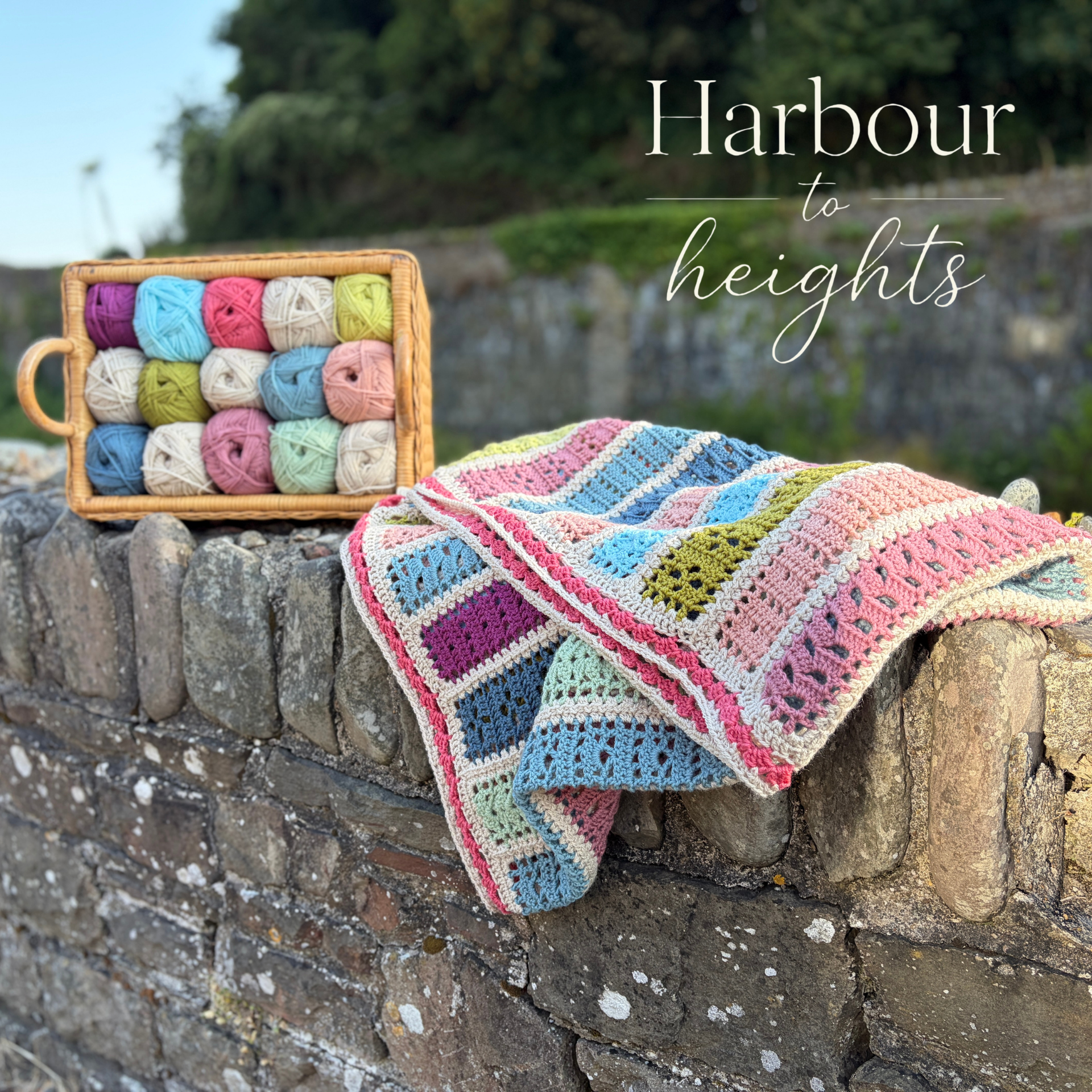 The harbour to heights blanket on a harbour wall with basket of yarn