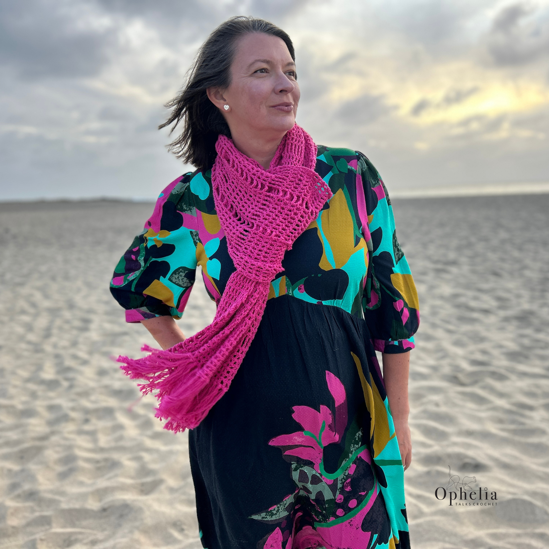 Raspberry pink crochet shawl styled as scarf with tassels, modern geometric lace wrap worn on beach at sunset, Ophelia Talks Crochet pattern