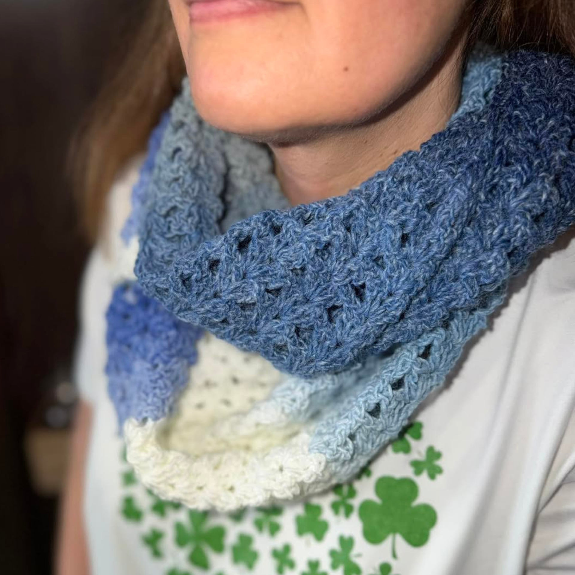 Crocheted infinity scarf in Curiosity yarn shade Ocean, featuring soft gradient tones from deep denim blue to pale sky blue and cream, worn around the neck to show textured stitch detail and cozy drape.