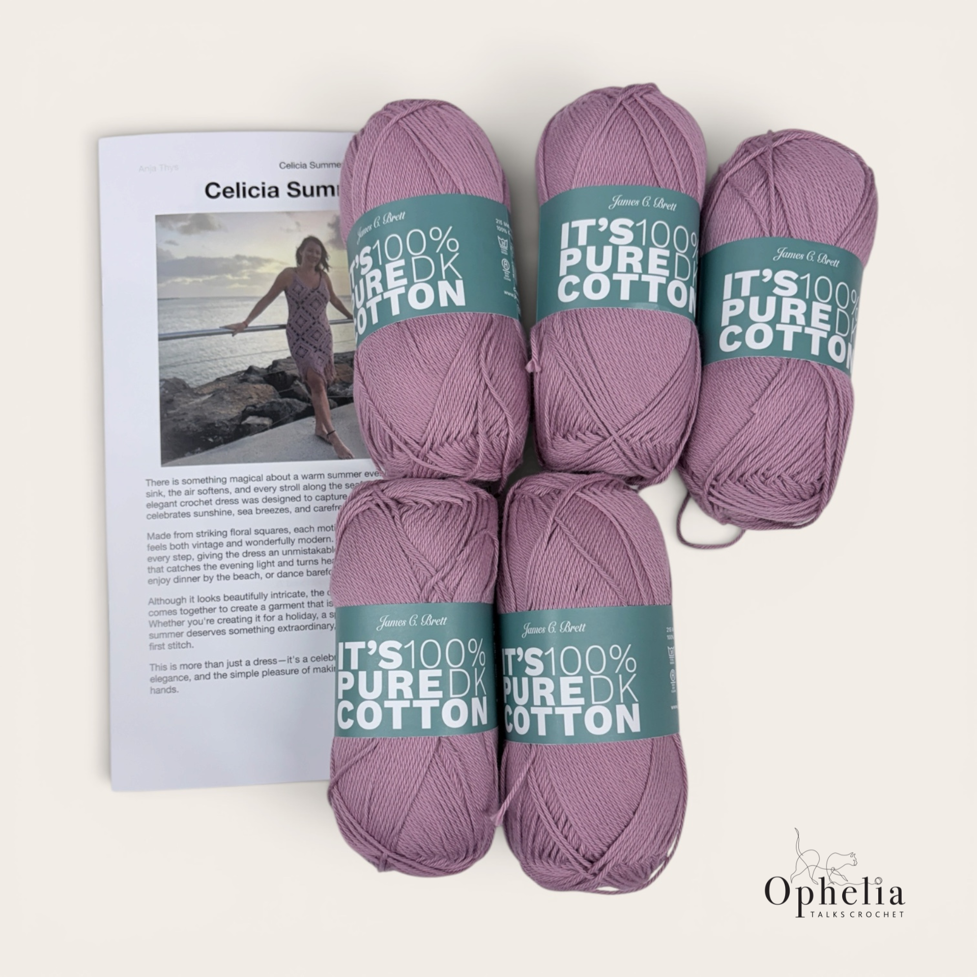 Five balls of James C. Brett It's 100% Pure Cotton DK yarn in a dusky mauve pink, arranged on a cream background beside a printed copy of the Celicia Summer Dress crochet pattern by Anja Thys. The pattern's cover photo shows a woman in a lilac crochet dress made from diamond floral motifs, standing on rocks by the sea at sunset. The Ophelia Talks Crochet logo appears in the bottom right corner.