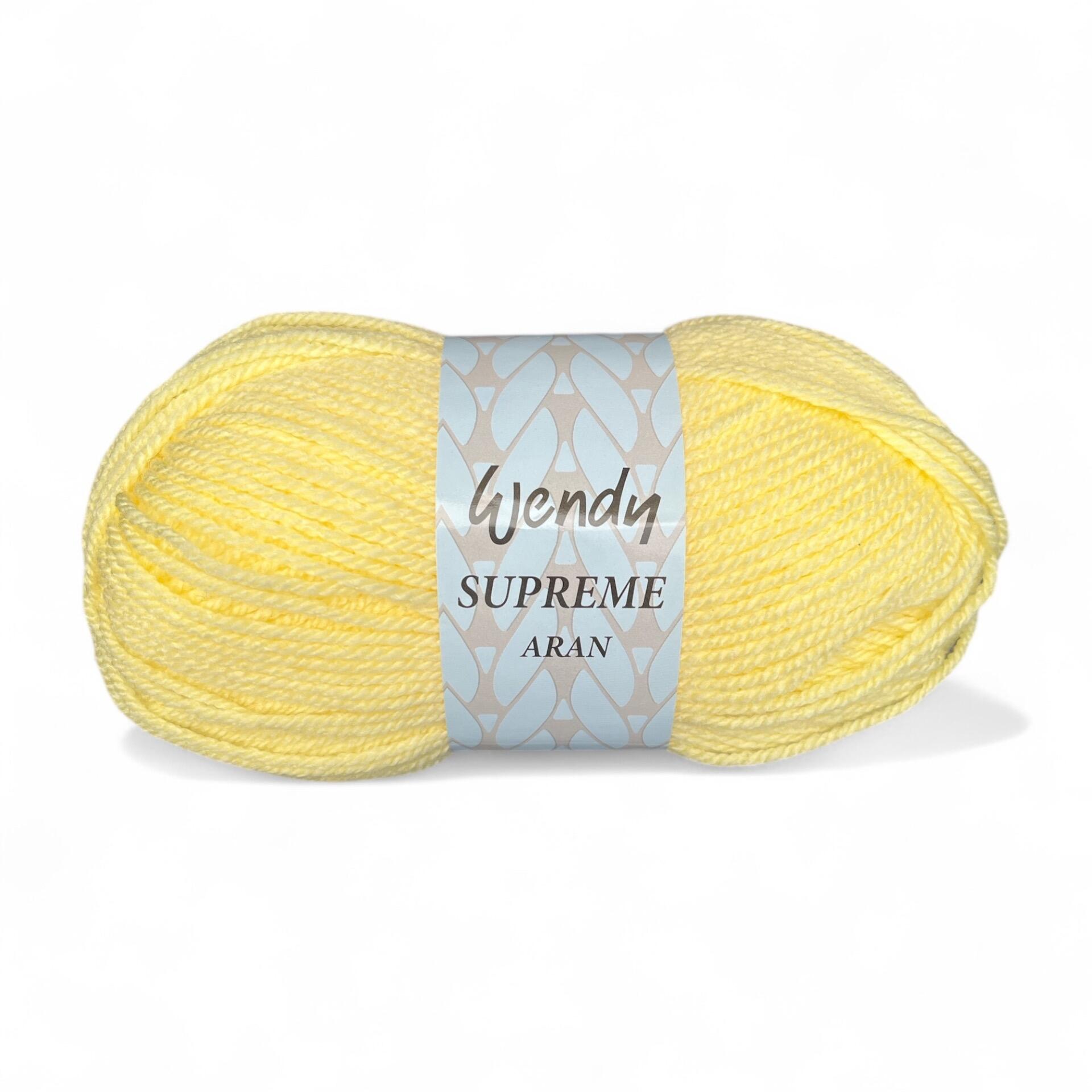 A skein of Wendy Supreme Aran yarn in Lemon (SA20), a light, cheerful yellow shade, wrapped in its branded label, displayed against a white background. The label features the "Wendy Supreme Aran" name with a decorative pattern.