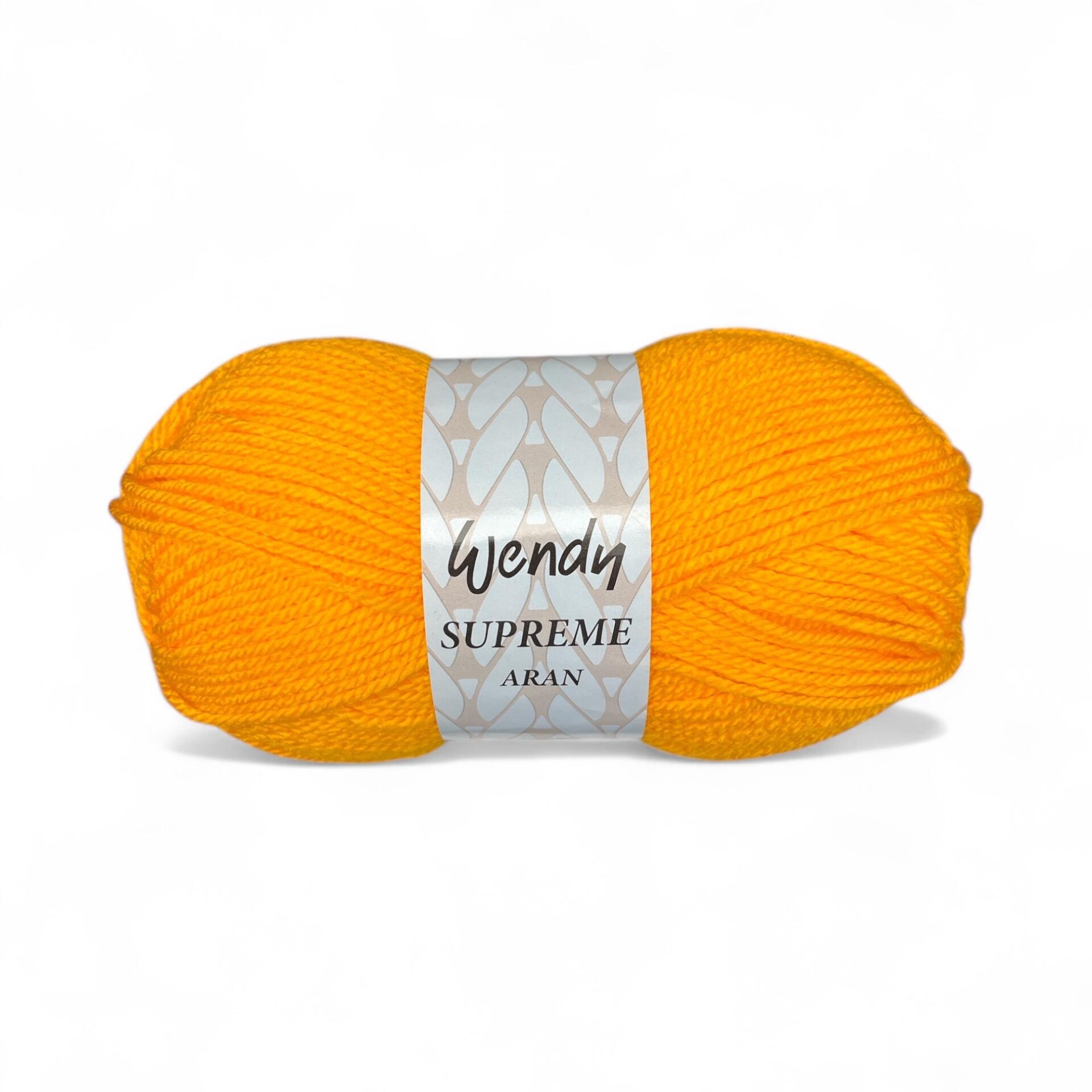 A skein of Wendy Supreme Aran yarn in Sunshine (SA22), a vibrant golden yellow shade, wrapped in its branded label, displayed against a white background. The label features the "Wendy Supreme Aran" name with a decorative pattern.