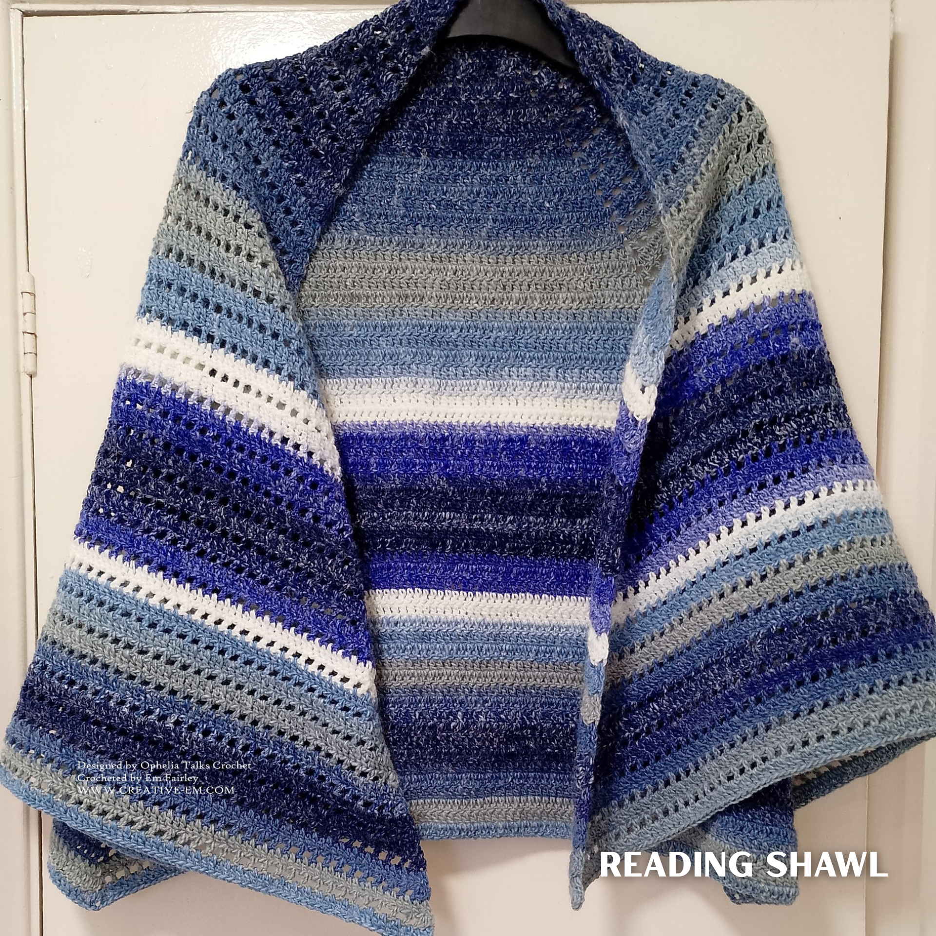 Customer-made Reading Shawl crochet pattern worked in Curiosity yarn shade Ocean, featuring horizontal stripes in deep blue, navy, grey, and white, with an airy textured stitch pattern and soft drape, hanging on a hanger.