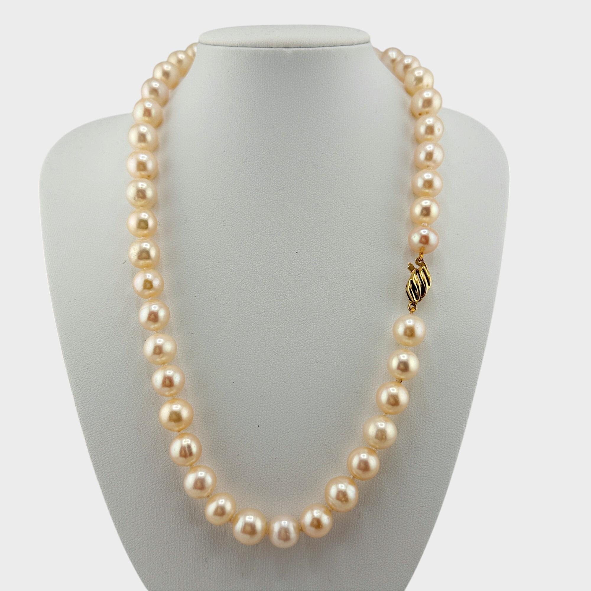 Elegant 17-inch cultured pearl necklace with oval 18K gold clasp, displayed on white breast.