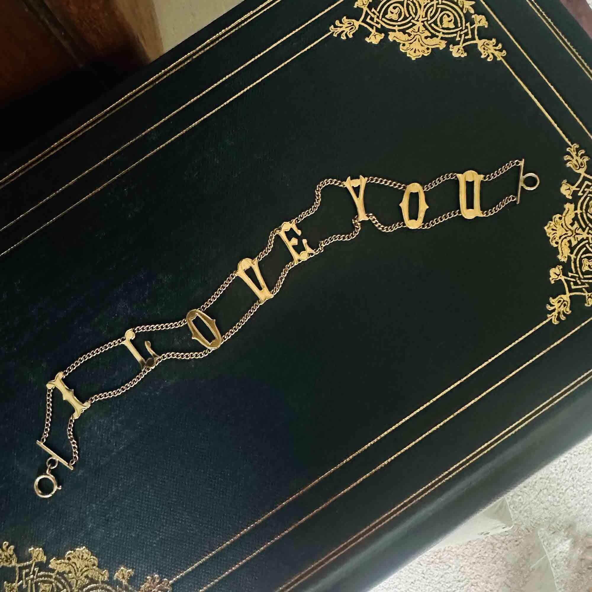 Vintage 9ct gold bracelet with "I Love You" links, layed flat on antique book.