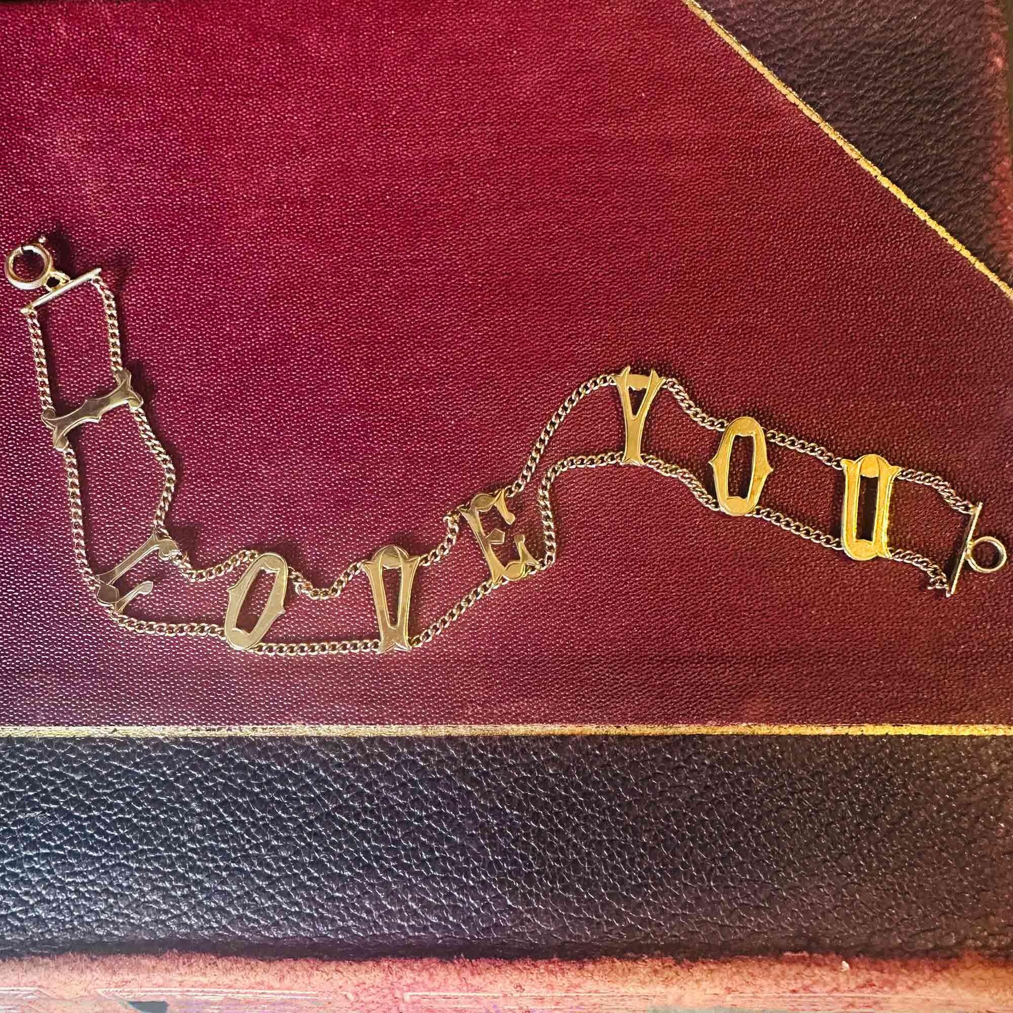 Vintage 9ct gold bracelet with "I Love You" links, layed flat on antique book.