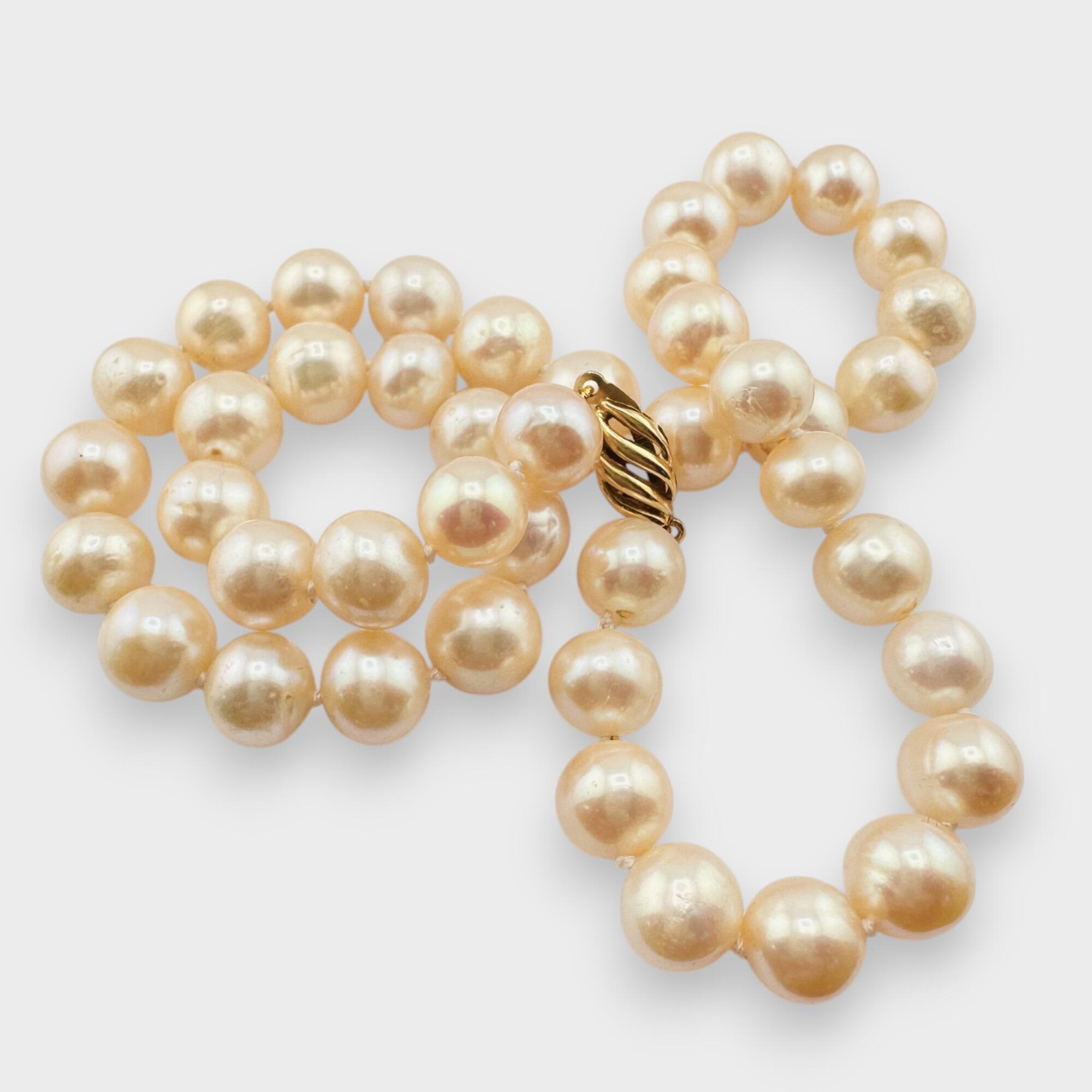 Elegant 17-inch cultured pearl necklace with oval 18K gold clasp, grey background.