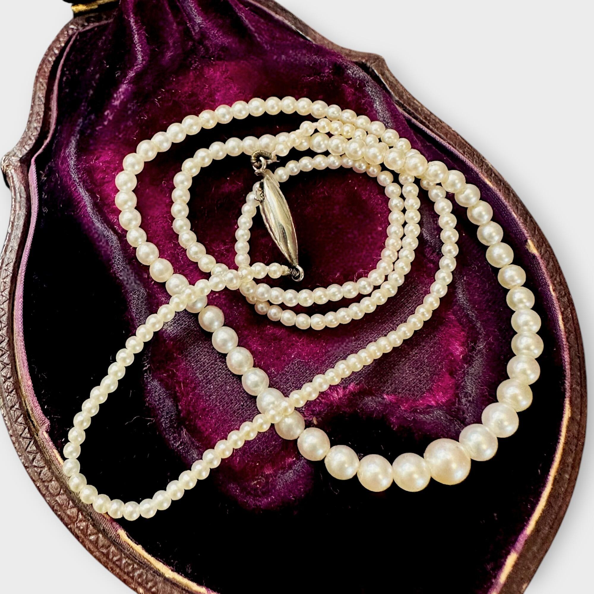 A row of akoya saltwater cultured pearls with 9k white gold torpedo clasp displayed on antique box.