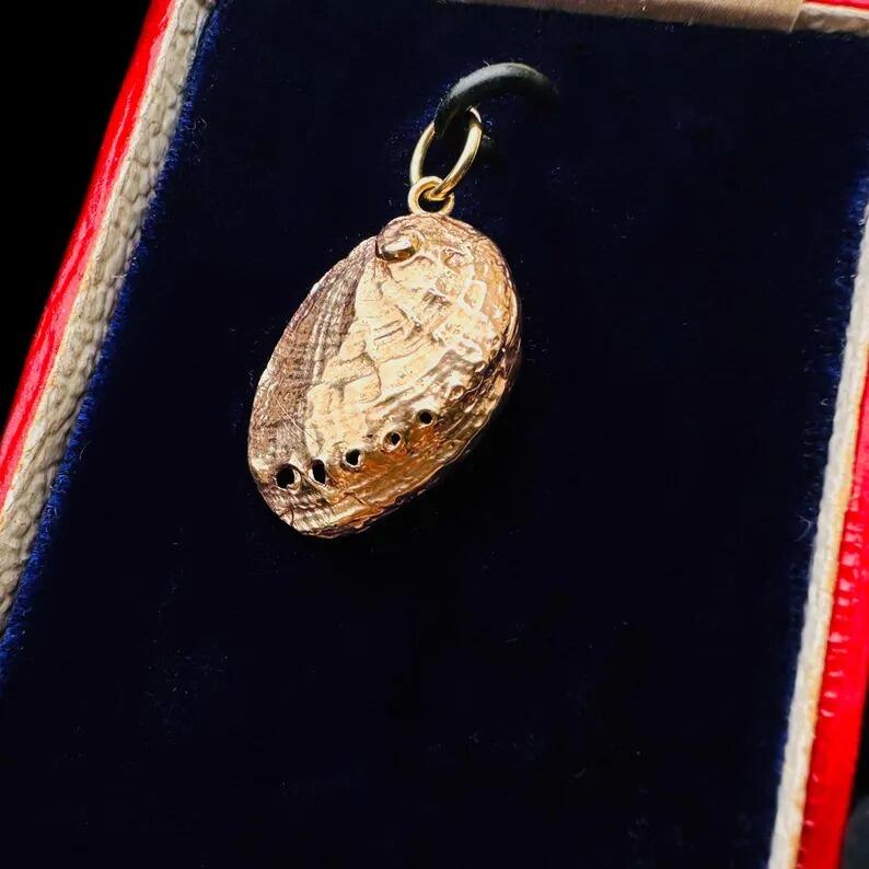 side view of Vintage 9ct Rose Gold Ormer Shell Pendant | Double Sided Sea Snail Charm displayed on antique box