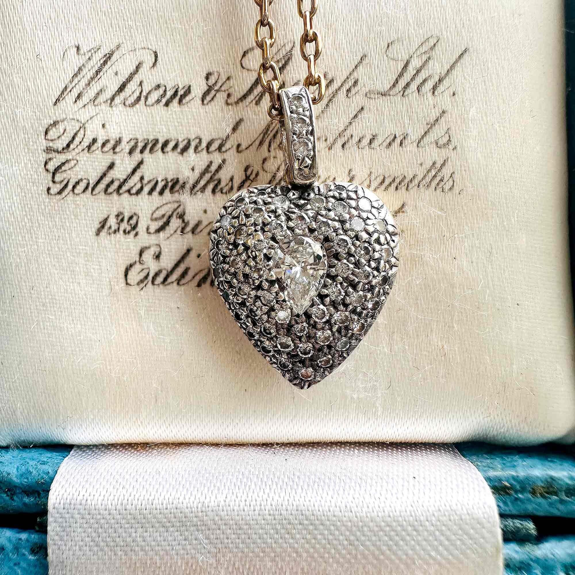 Diamond Heart Locket Pendant with Pear-Shaped Center displayed on a antique box