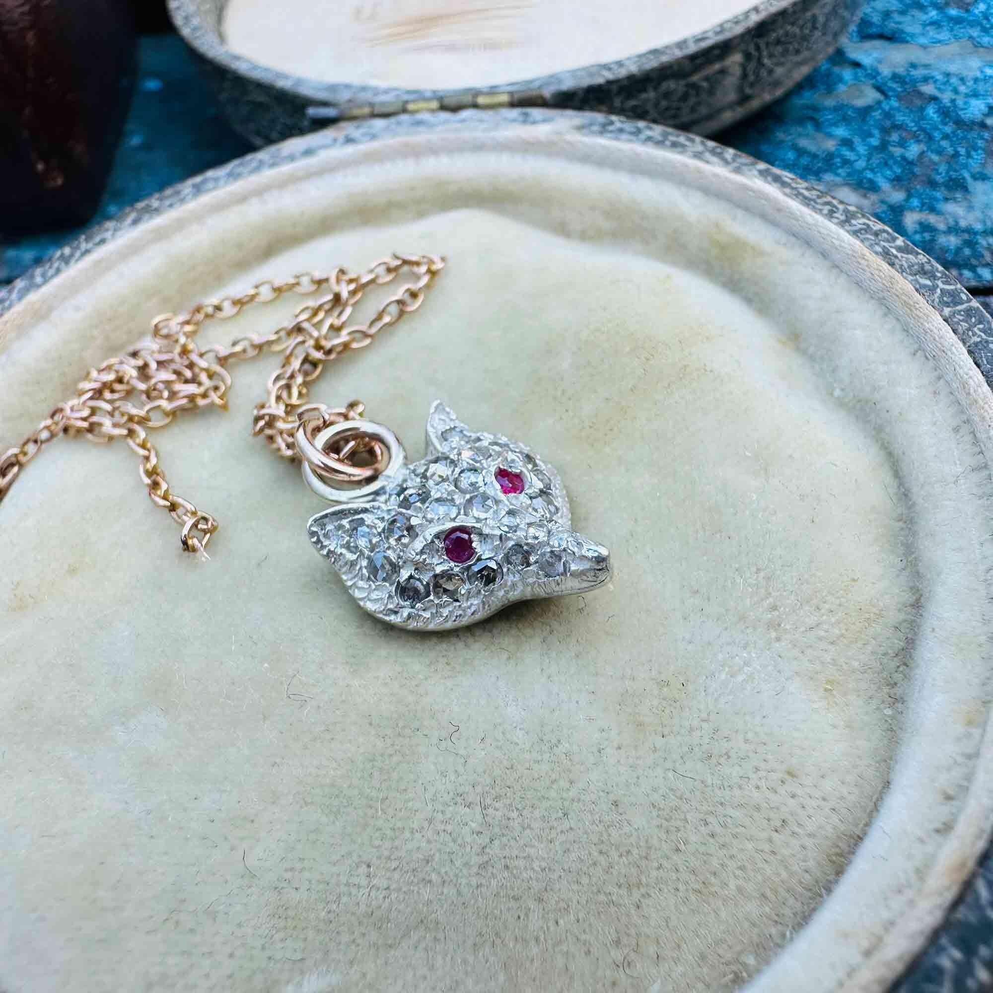 side view of Vintage Fox Head Pendant: Rose Cut Diamonds, Ruby Eyes, Silver & 9ct Rose Gold displayed on antique box